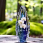 een blauwe glazen urn met een afbeelding van een witte orchidee en een naam in zilver sign folie