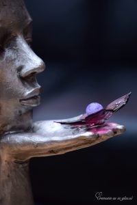 het beeld met een tedere kus laat ik je vrij van een beeld met op haar hand een glazen vlinder en een mini urn van glas met crematie-as