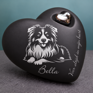 Matzwarte keramische harturn met een zilverkleurige afbeelding van een liggende bordercollie, de voorbeeldnaam Bella, het opschrift ‘Voor altijd in mijn hart’ en een metalen hartje.